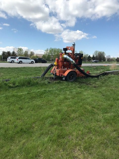 a red booster pump sits in the grass with its black pumps out in front of a road with cars