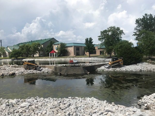 gray rocks line the edges of a small pond to prevent erosion